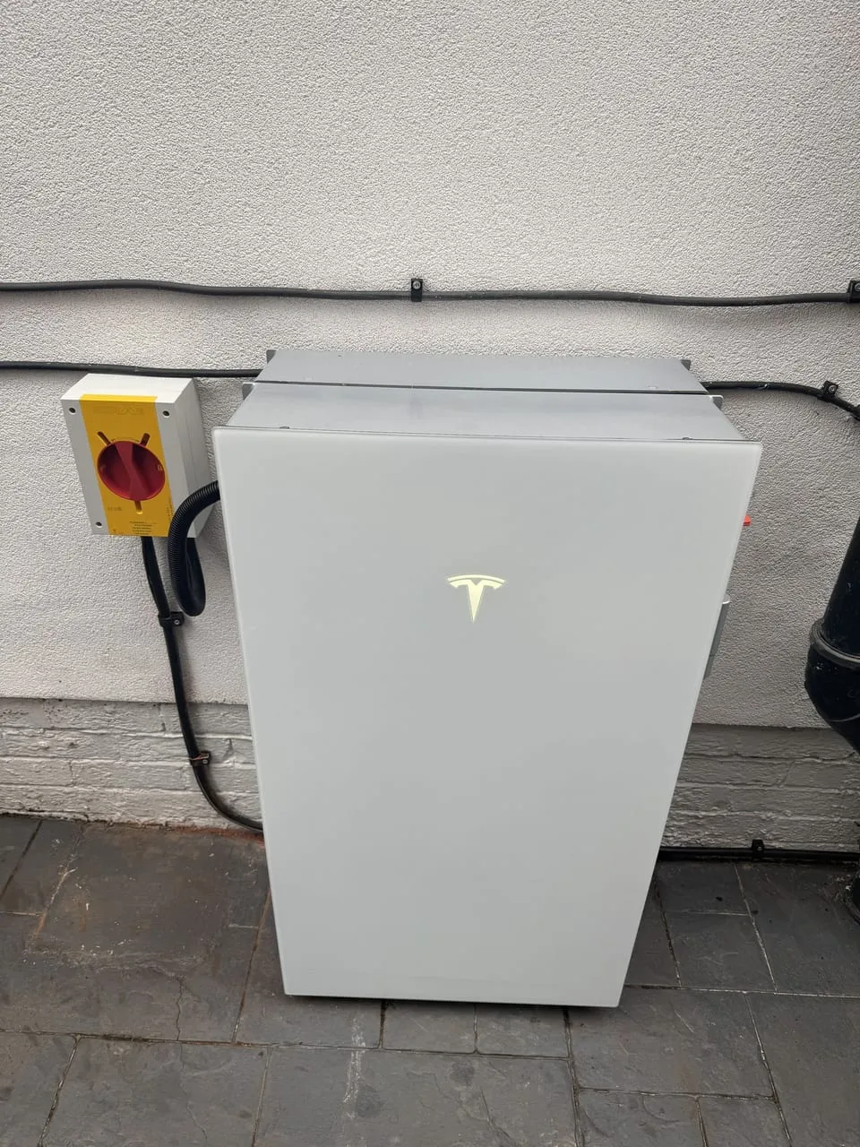 A Tesla Powerwall home battery wall-mounted beside an isolator switch