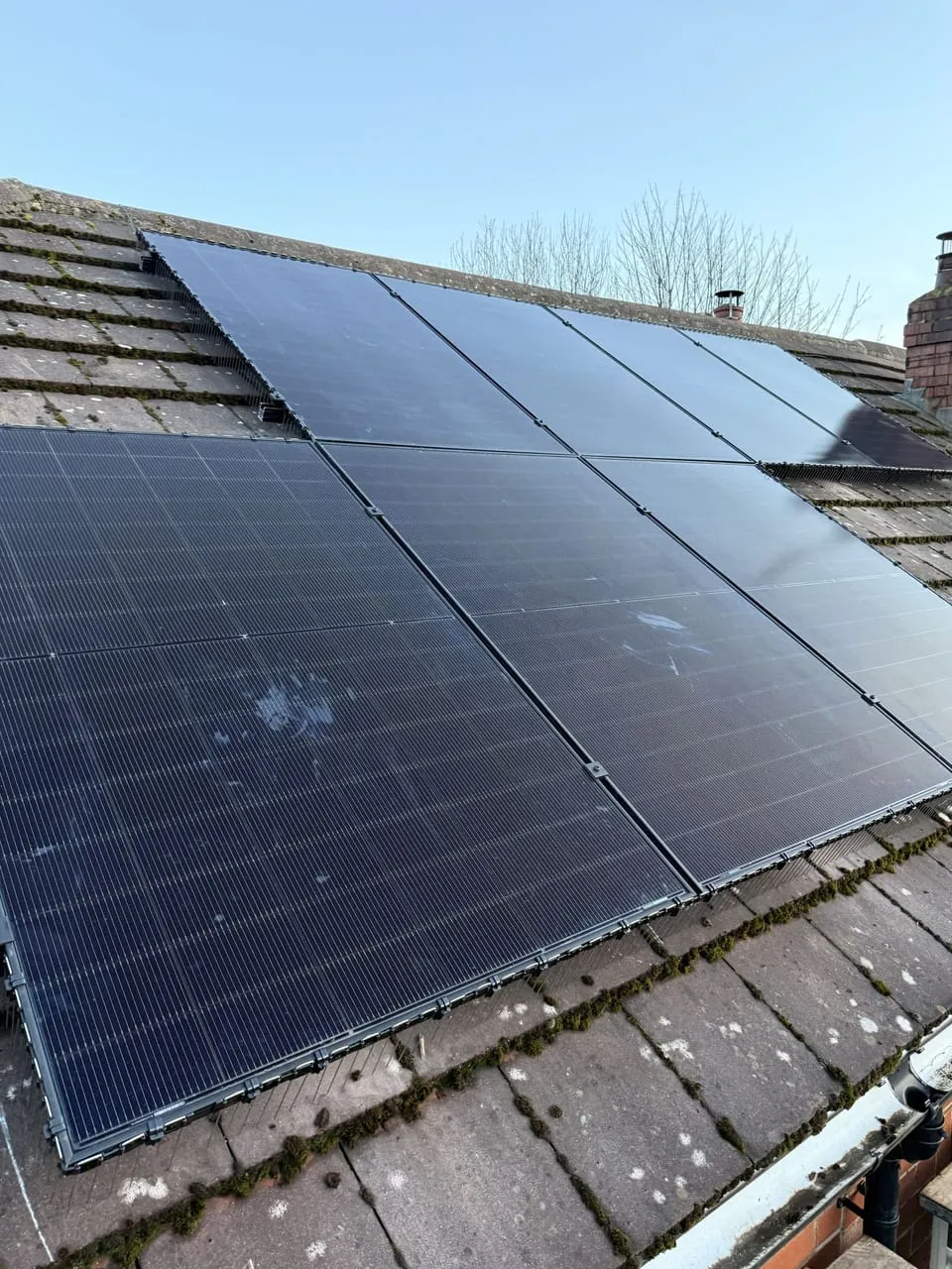 Black solar panels installed across a UK tiled house roof under blue sky
