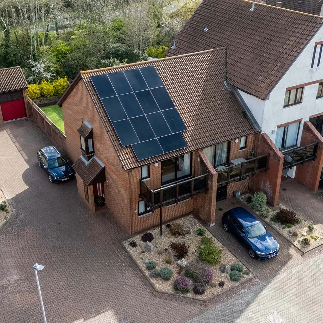 Aerial view of black solar panels on a UK brick house with cars on the drive